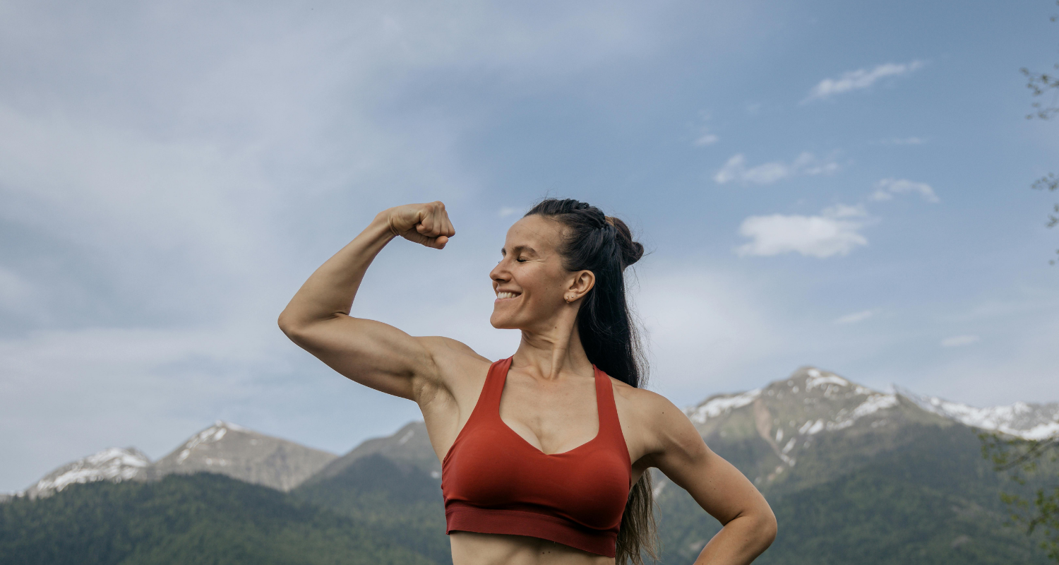 Woman flexing her arm muscles with mountains in the background